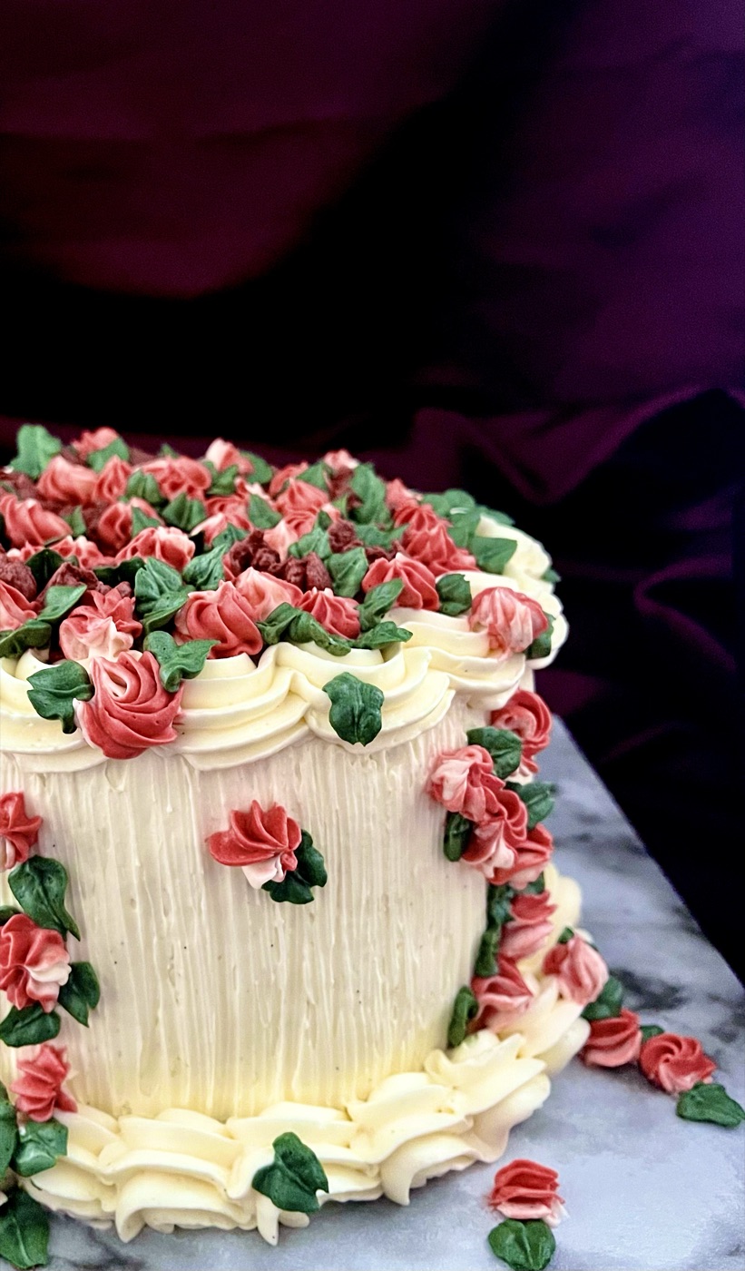 Cream buttercream cake topped with pink and green piped roses on a marble board